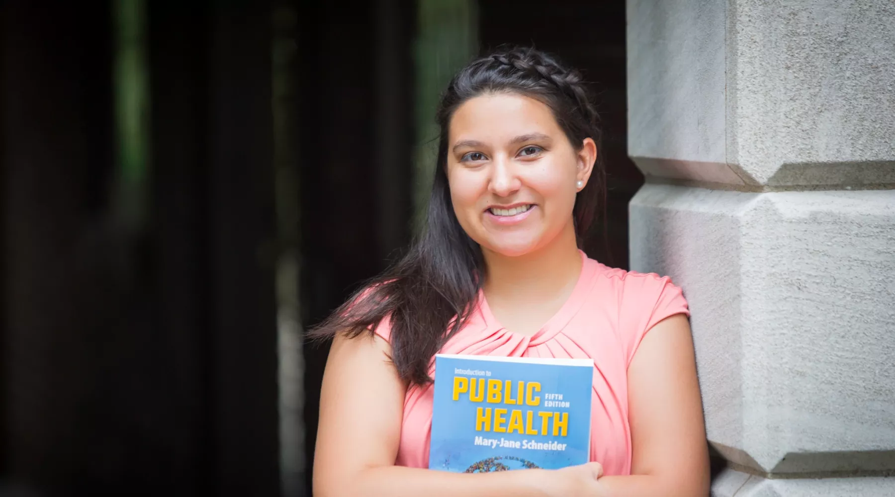 Student smiling holding Public Health textbook
