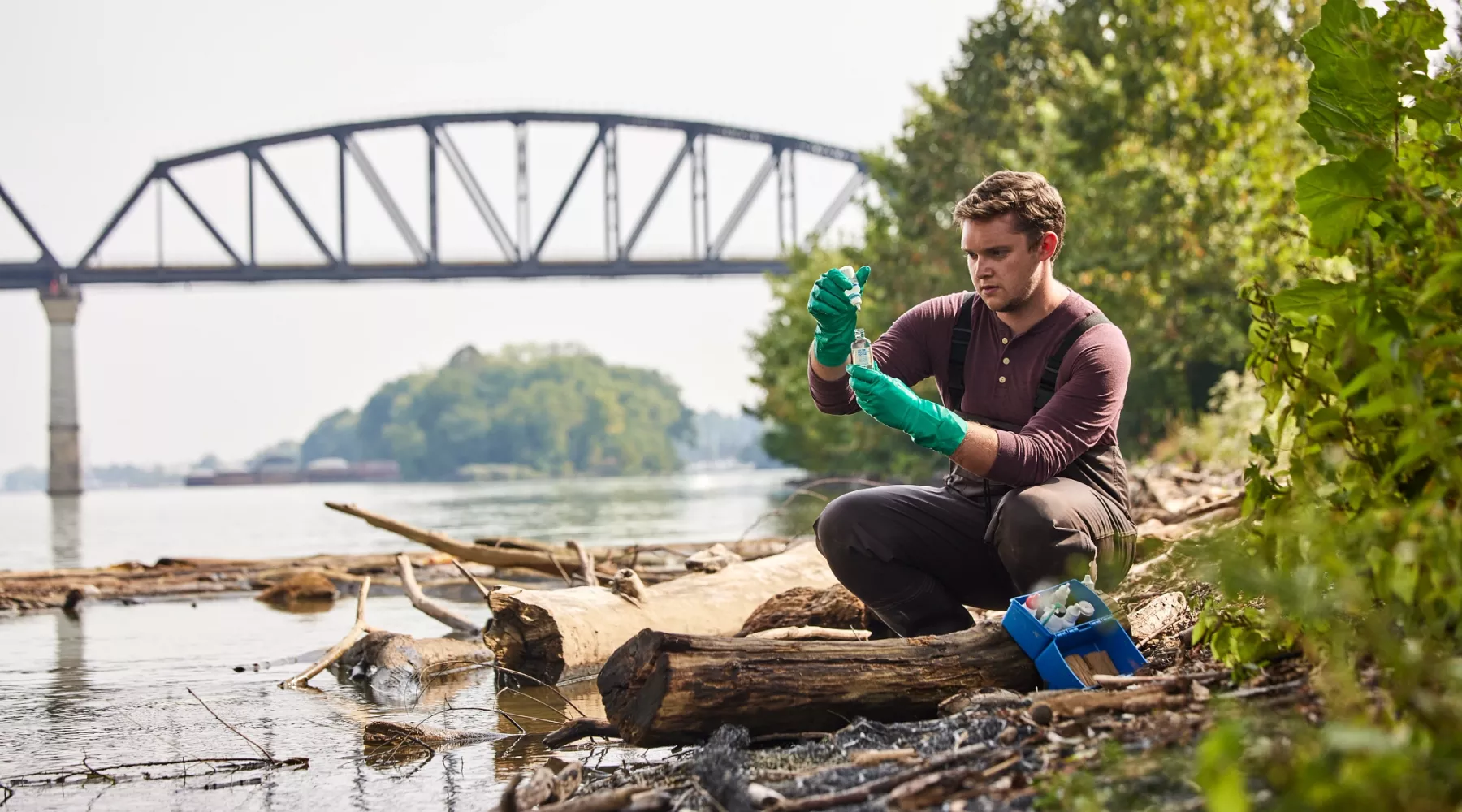 Sam Kessler is testing the water at the Ohio river as he sits close to the edge of the river to retrieve and test the sample.