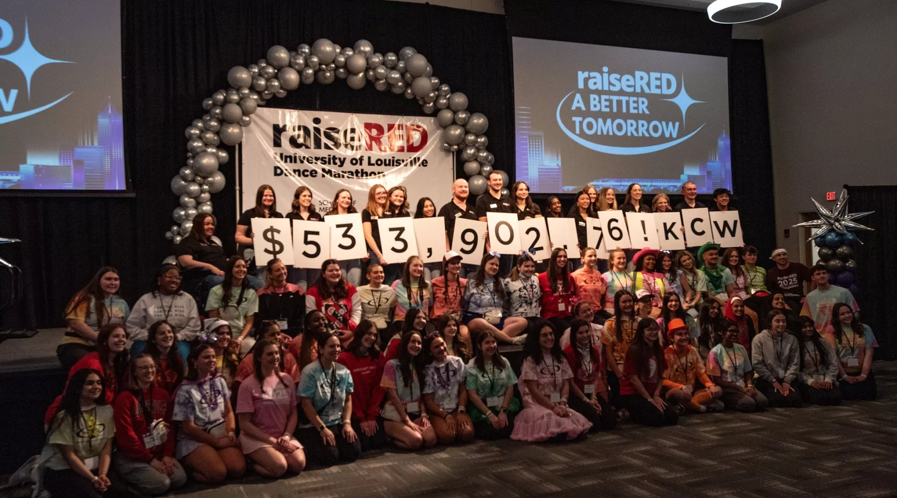 Students hold up white cards that show $533,902.79. Other students stand around cheering.